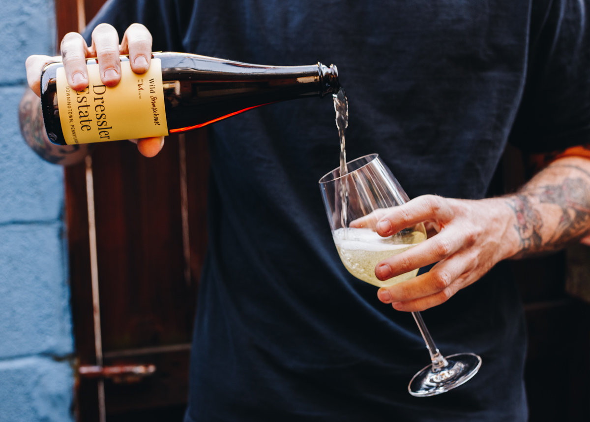 A man pours a 500 mL bottle of Dressler Estate's Wild Smokehouse cider into a glass.
